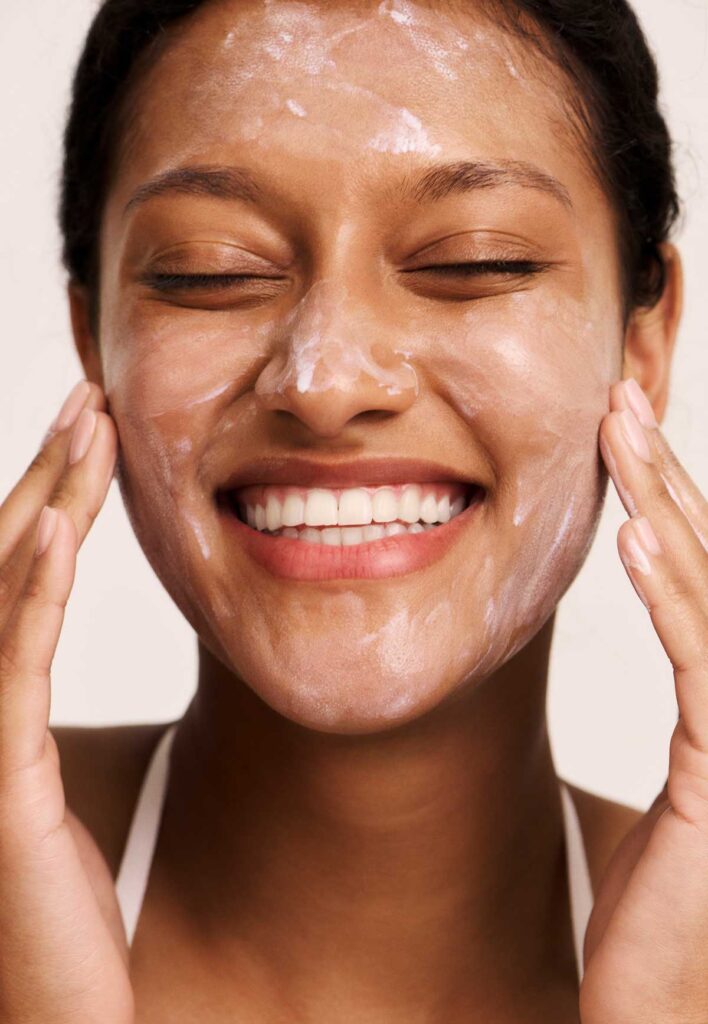 A young, smiling Black woman gently exfoliating her skin