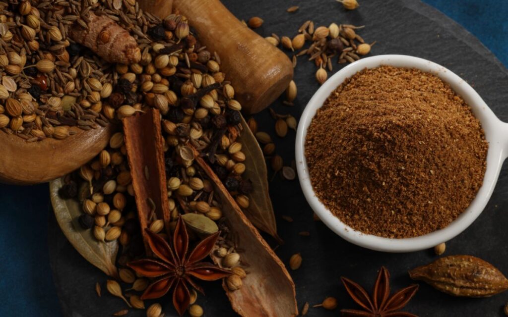 A spice bowl filled with garam masala surrounded by spices waiting to be ground