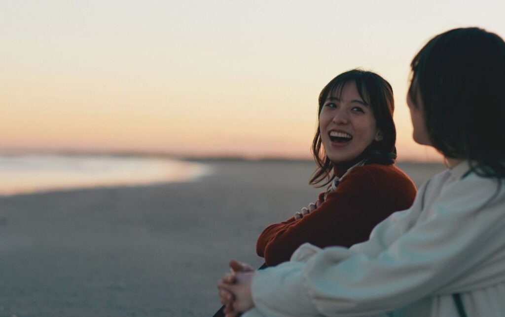 Two women talking and laughing on a beach at sunset
