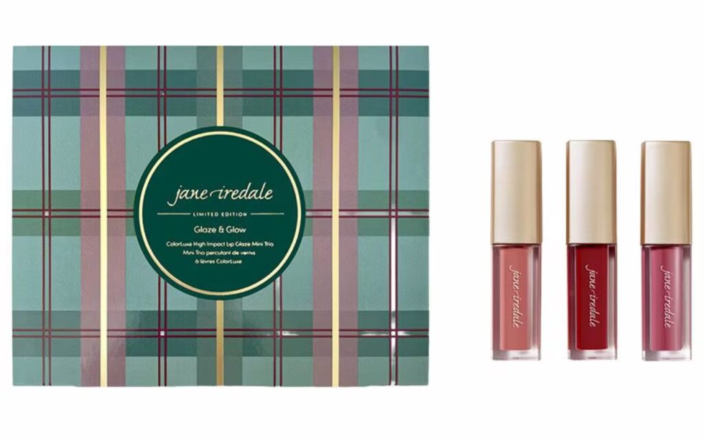 A Jane Iredale holiday beauty gift set in a plaid box; three red, coral and pink lip glosses are placed beside it.