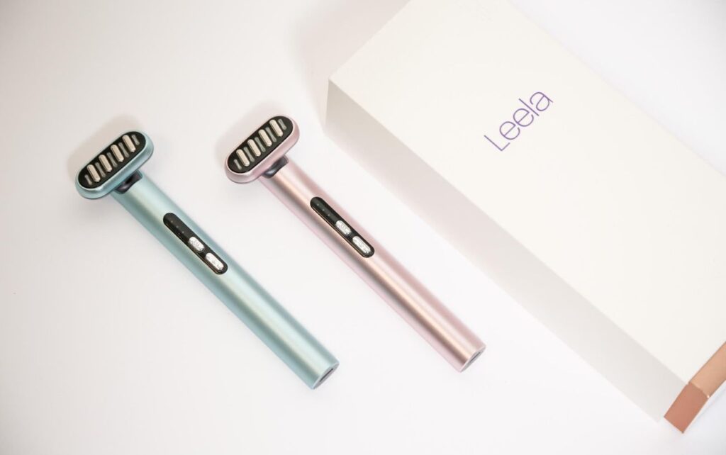 Ice blue and light pink Leela red light wands placed next to a Leela gift box.