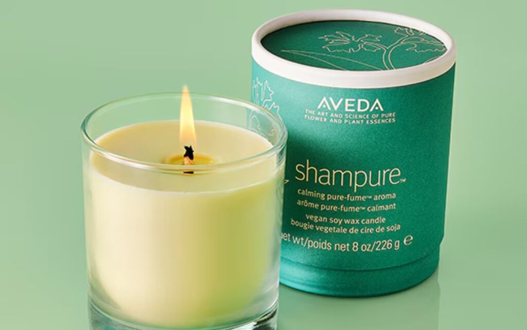 A vegan soy wax Aveda Shampure candle burning next to a round green candle box.